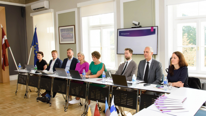 Attēlā attēlots delegācija, kas seiž sanāksmes zālē.